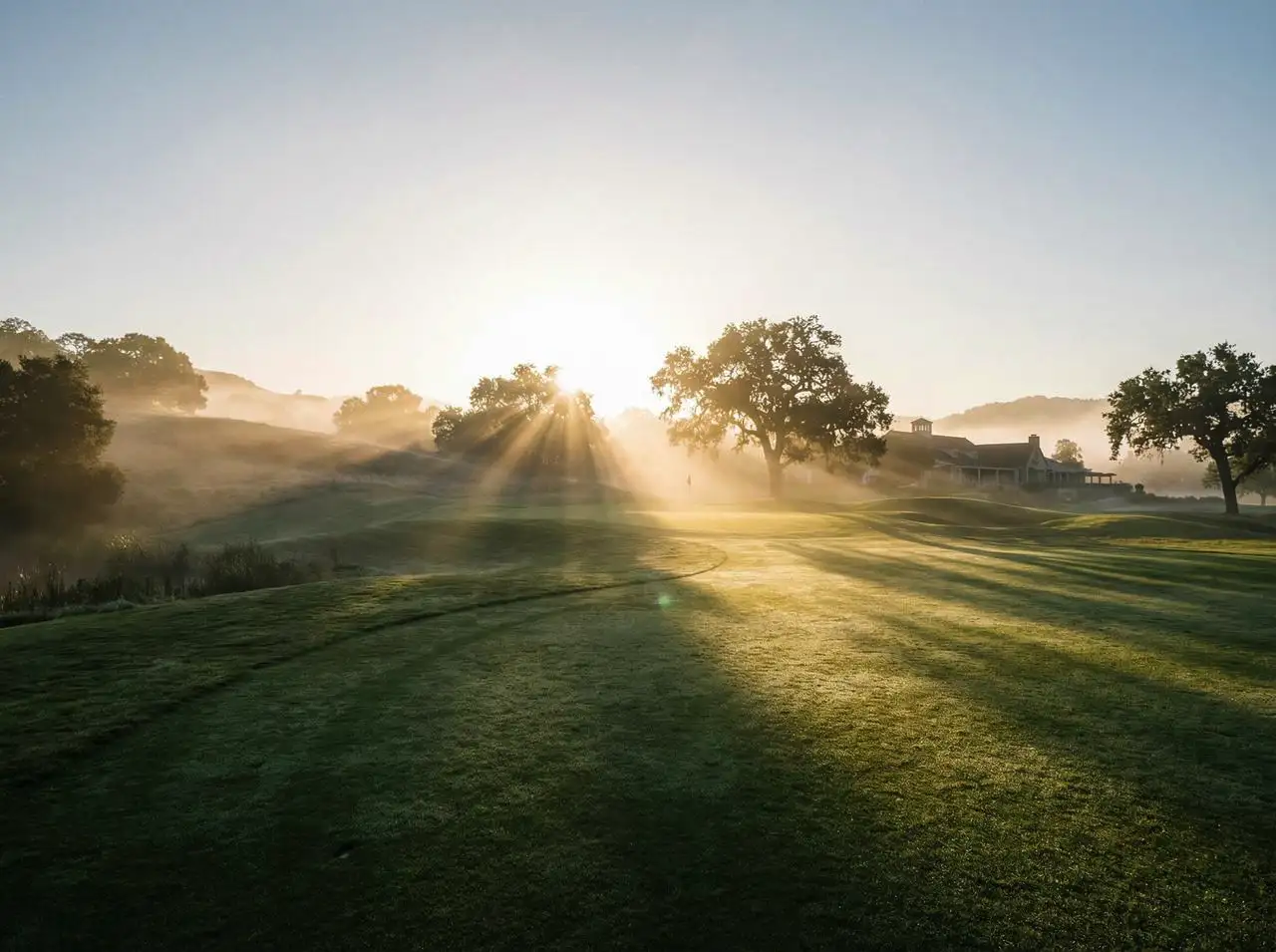 Sunrise over a misty golf course with golden rays illuminating the fairway, ultra‑realistic landscape photography.
