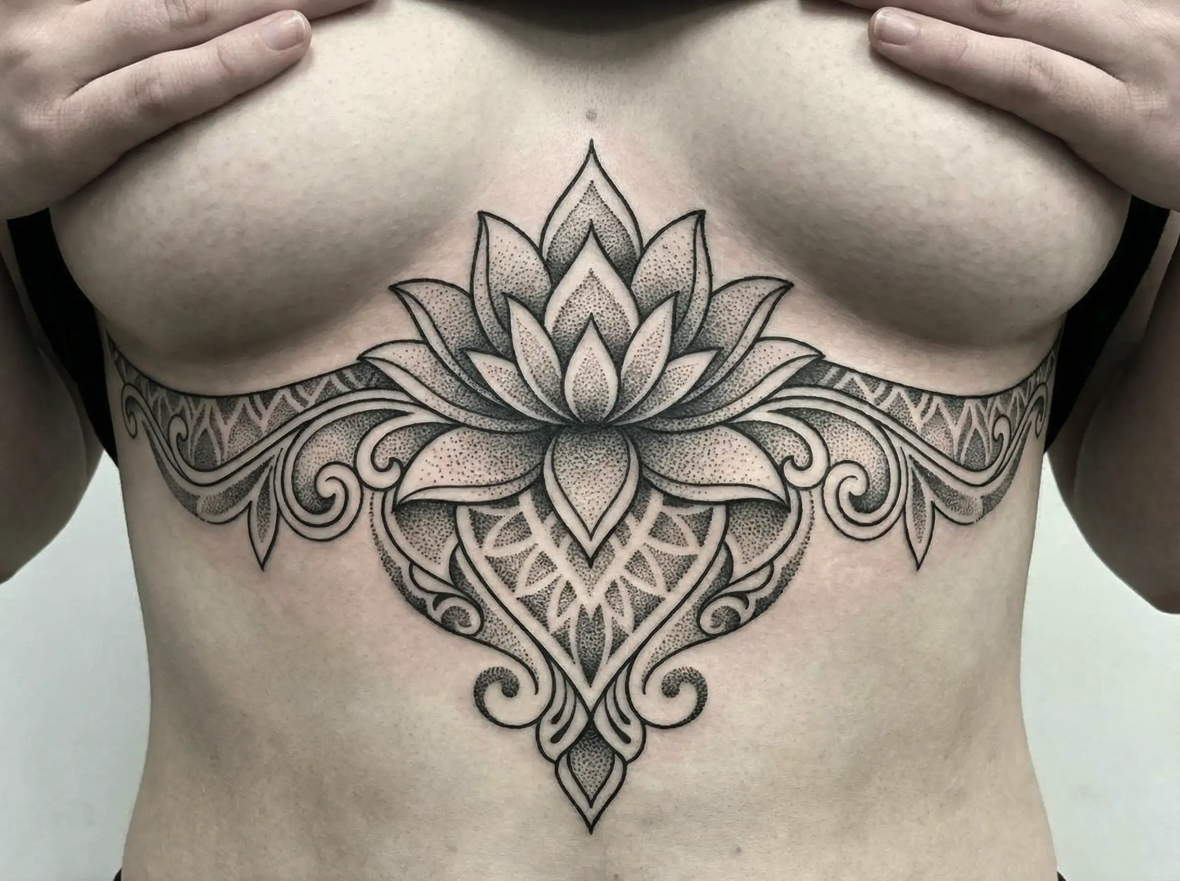 وشم لوتس مصمم لوضع على عظمة الصدر، خطوط زخرفية ممتدة على الجوانب، نقط صغيرة خفيفة للملمس، هيكل أنيق ومتوازن جيدًا.