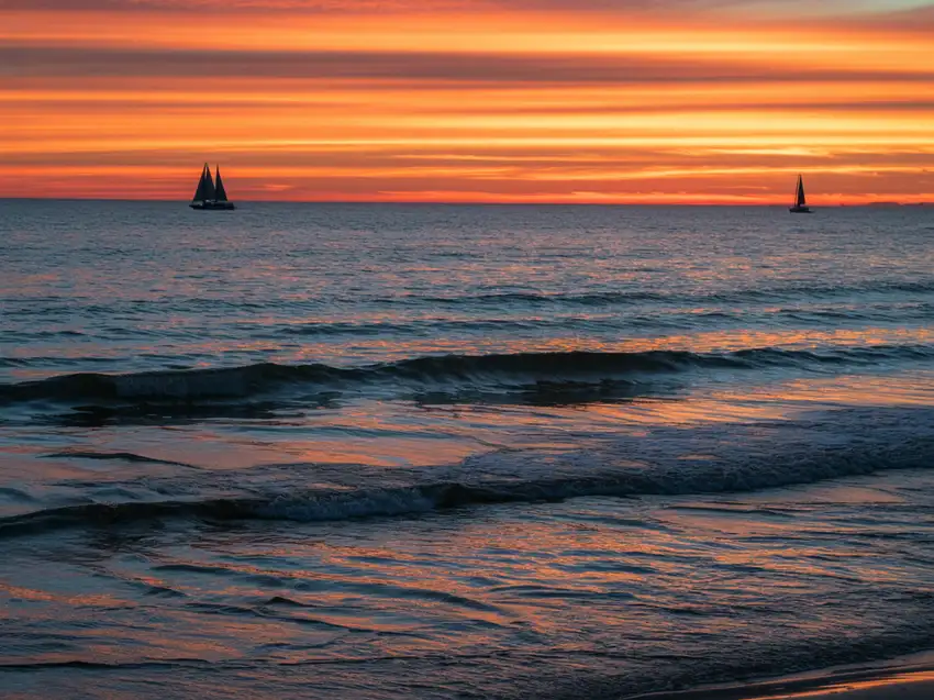 Orange sunset over calm ocean waves, glowing horizon, soft reflections on water, cinematic wide-angle scene.