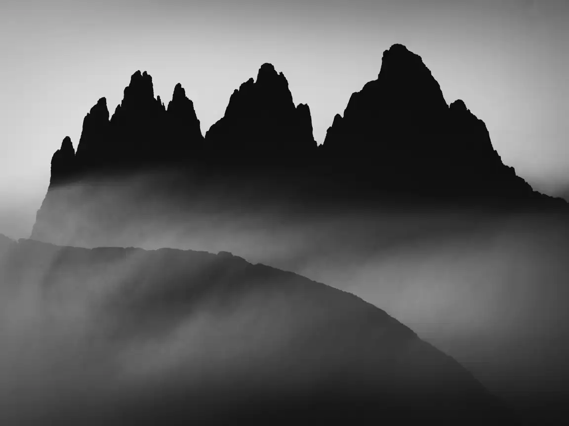 Minimalist black and white mountain silhouette with soft fog layers, high contrast, clean negative space, ultra-wide wallpaper composition.